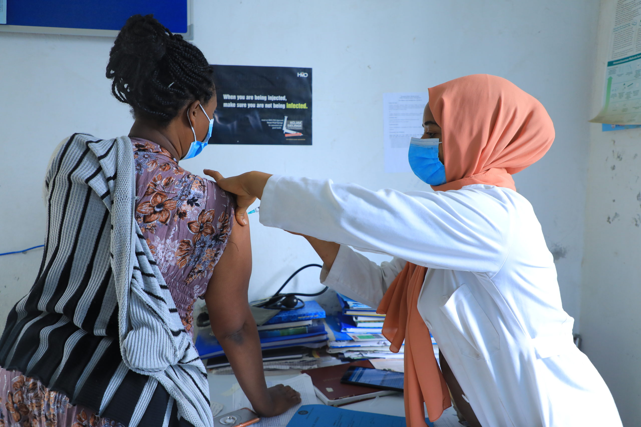 medical professional wearing a headscarf is administering an injection for a female patient